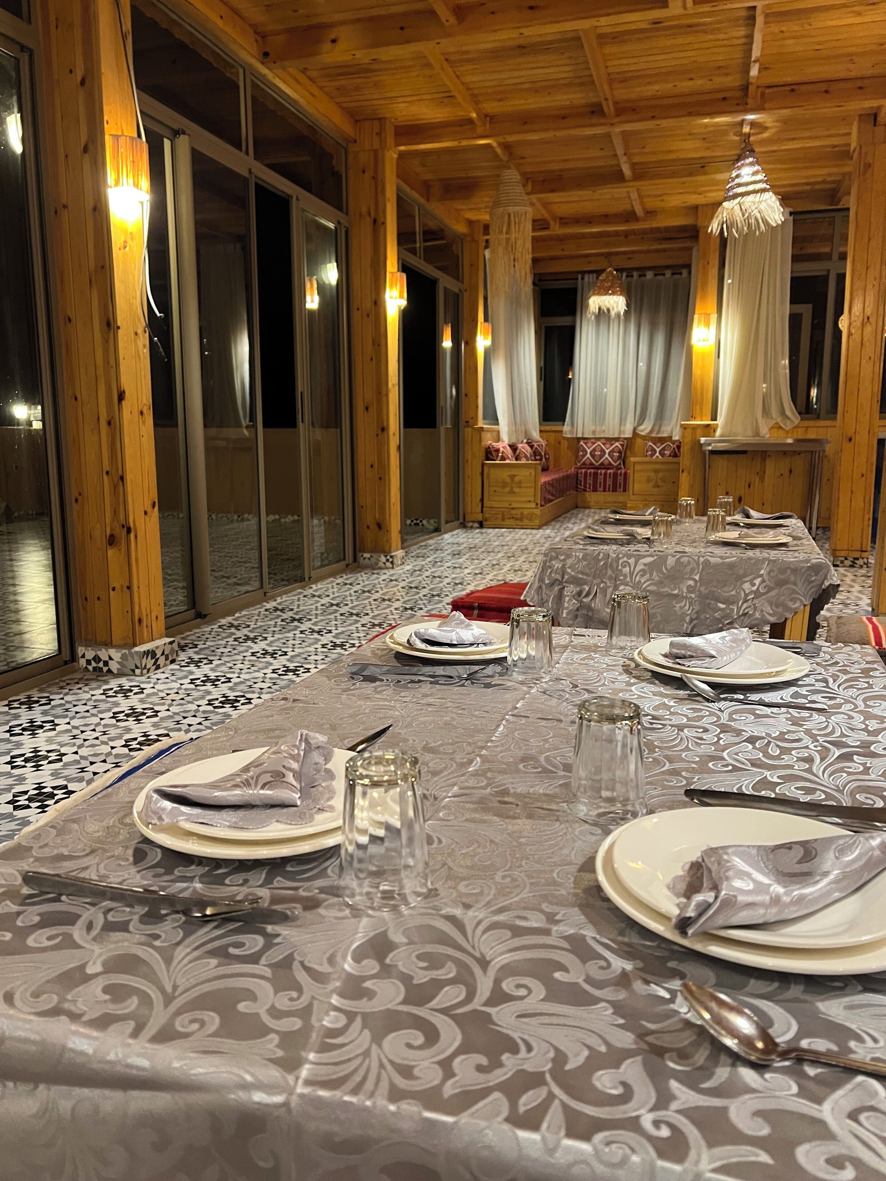 A dining area with a long table set for a meal, wooden walls, and large windows.