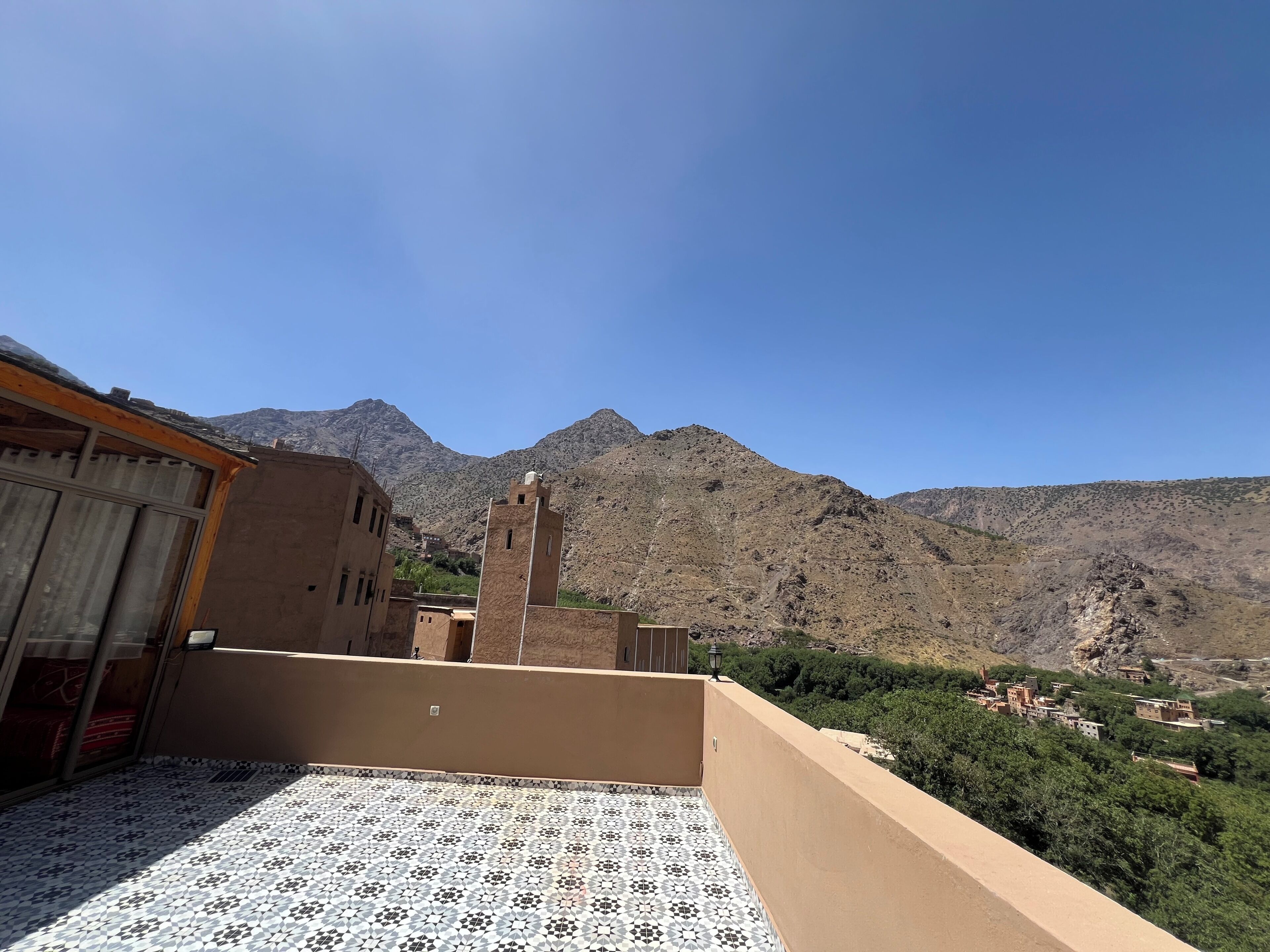 Une terrasse sur le toit ornée de carreaux décoratifs, une vue sur un paysage montagneux et un bâtiment doté d’une tour.
