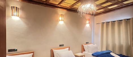 A hotel room with three beds, each with a blue bedspread, wooden headboards, and bedside tables with lamps.