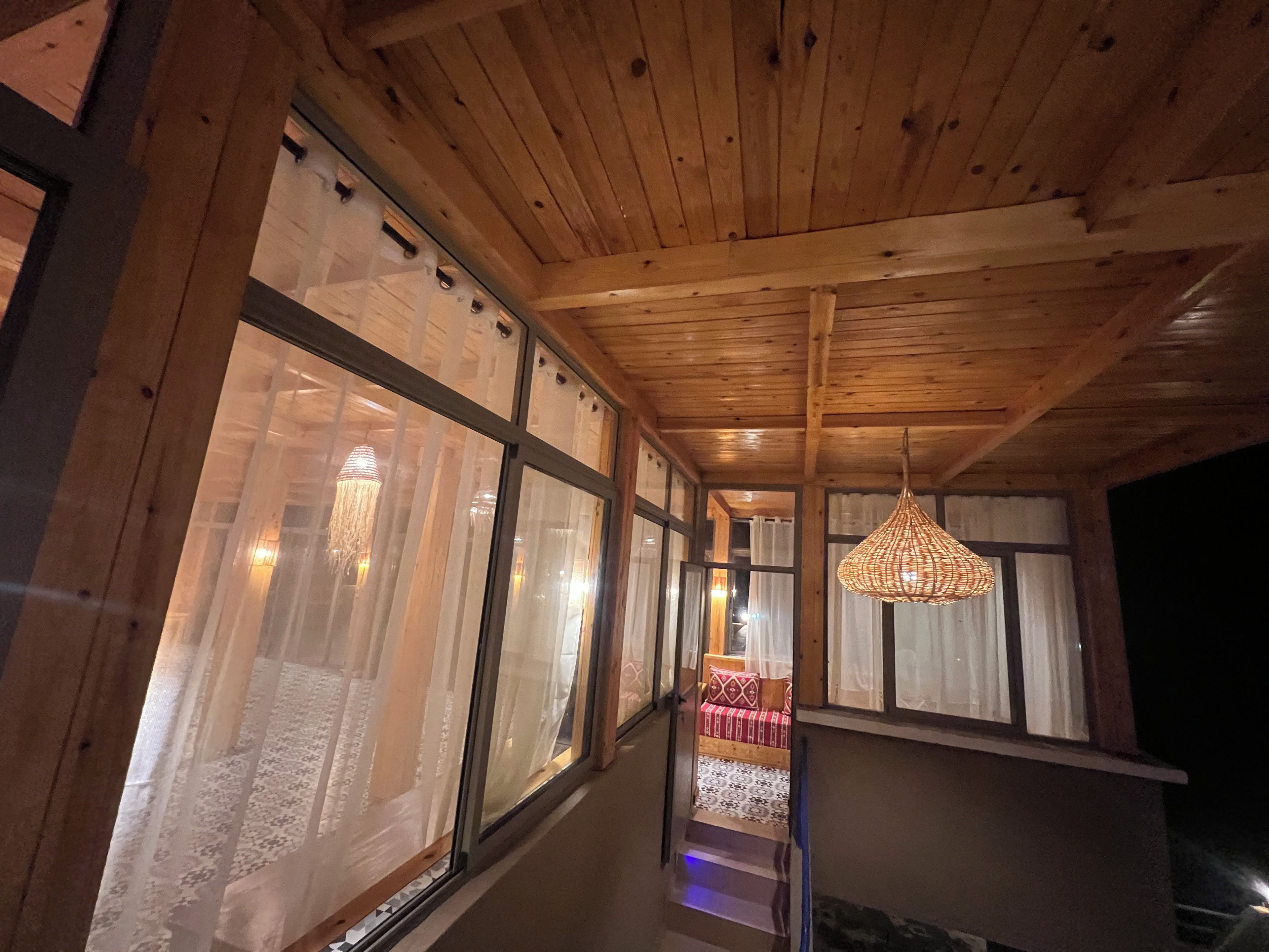 Un couloir doté d’un plafond en bois et de grandes fenêtres, qui mène à une pièce comprenant un lit et un luminaire suspendu.