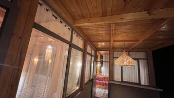 Un couloir doté d’un plafond en bois et de grandes fenêtres, qui mène à une pièce comprenant un lit et un luminaire suspendu.