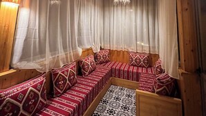 A wooden cabin interior with a long, narrow sofa set against a wall, a patterned floor, and a wooden ceiling.