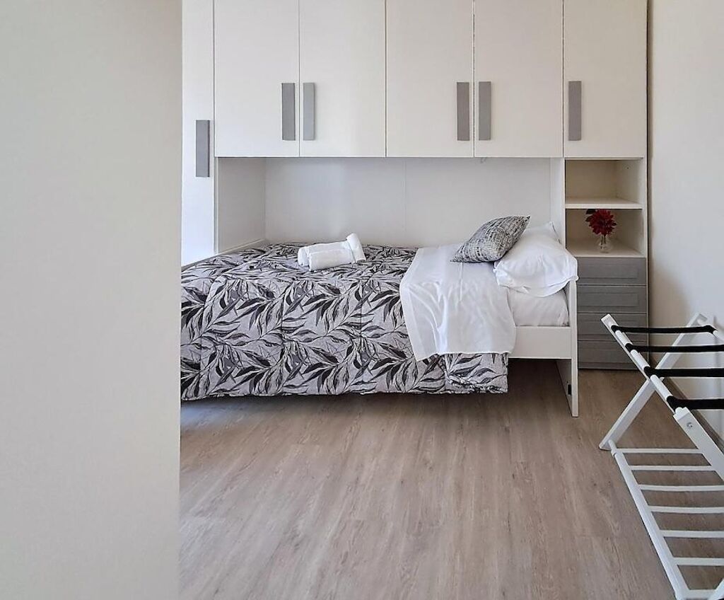 A bedroom with a bed, a white wardrobe, and a shelf with a vase.