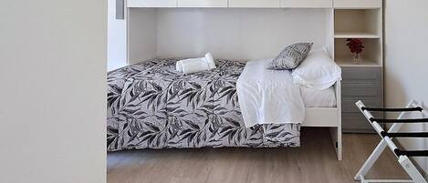 A bedroom with a bed, a white wardrobe, and a shelf with a vase.
