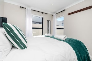 A hotel room with a bed, a window, a door, and a view of the outside.