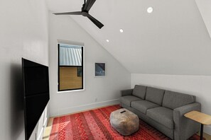 A modern living room with a grey sofa, a red patterned rug, a small round ottoman, a television, and a ceiling fan. - Larkspur Haven, luxury, close to trails & town of CB, has tennis, pickleball! (Crested Butte)
