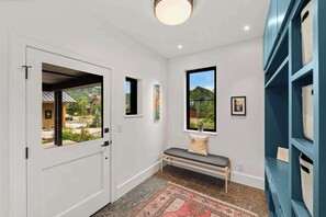 A hallway with a bench, a door leading outside, and a wall with a window and artwork. - Larkspur Haven, luxury, close to trails & town of CB, has tennis, pickleball! (Crested Butte)