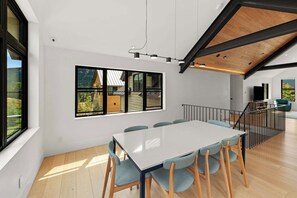 A modern dining area with a large table and chairs, a view of the outdoors through large windows, and a staircase leading to another level. - Larkspur Haven, luxury, close to trails & town of CB, has tennis, pickleball! (Crested Butte)