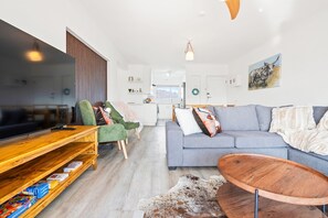 Una sala moderna con un televisor de pantalla plana, un sofá, una mesita de centro y un estante de madera con libros.