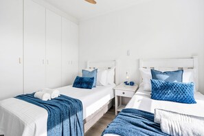 Een hotelkamer met twee bedden, elk voorzien van een witte hoofdbord, een nachtkastje en een blauwe deken.