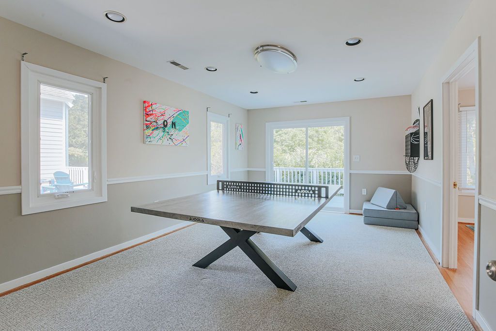 A room with a ping pong table, windows, and artwork on the walls.