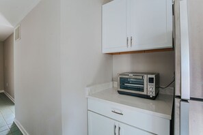 Una cocina con gabinetes blancos, horno tostador empotrado y refrigerador de acero inoxidable.