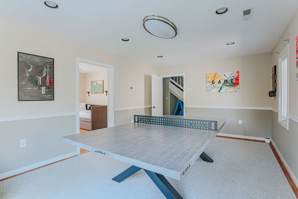 A room with a ping pong table, a framed picture on the wall, and a staircase in the background.