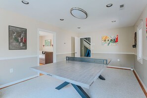 Una habitación con mesa de ping pong, un cuadro en la pared y una escalera al fondo.