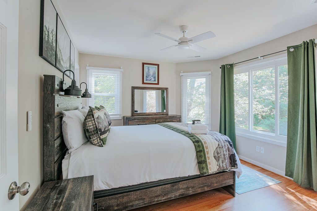 A bedroom with a bed, a ceiling fan, a dresser, a mirror, and a window with curtains.