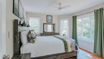 A bedroom with a bed, a ceiling fan, a dresser, a mirror, and a window with curtains.