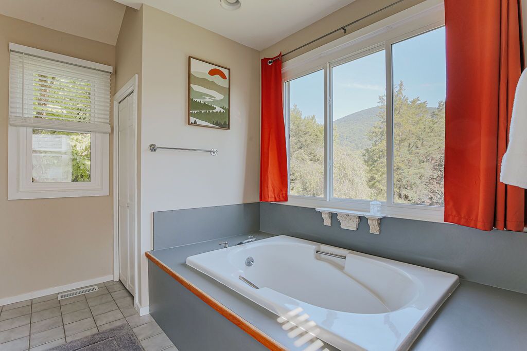 Un baño con una bañera grande, una ventana con cortinas y un perchero para toallas.