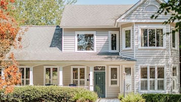 A two-story house with a front porch, a green door, and a small front yard.