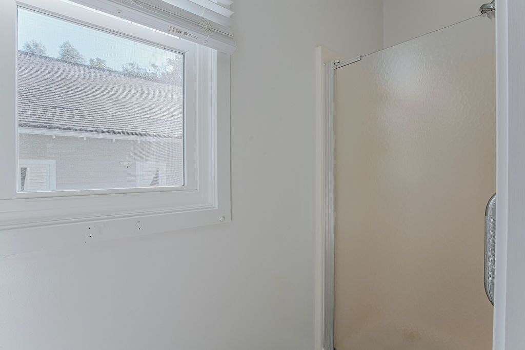 A bathroom with a window, a shower, and a door.