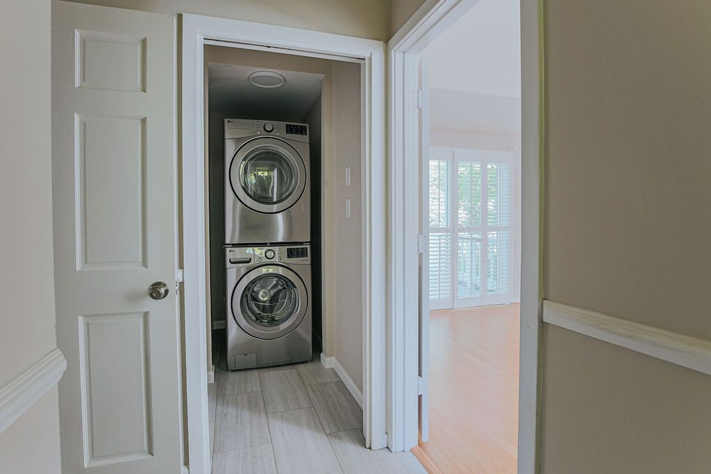 A laundry room with two stacked washing machines and a door leading to a balcony.