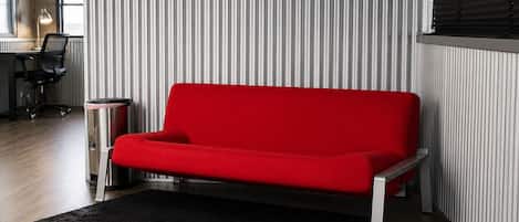 A modern living room with a red sofa, a black rug, and a striped wall.