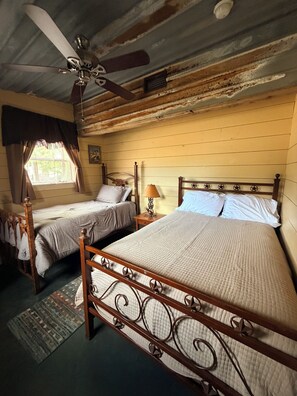 Ein Zimmer mit zwei Betten, einem Deckenventilator, einem Fenster mit Vorhängen und einem Teppich.