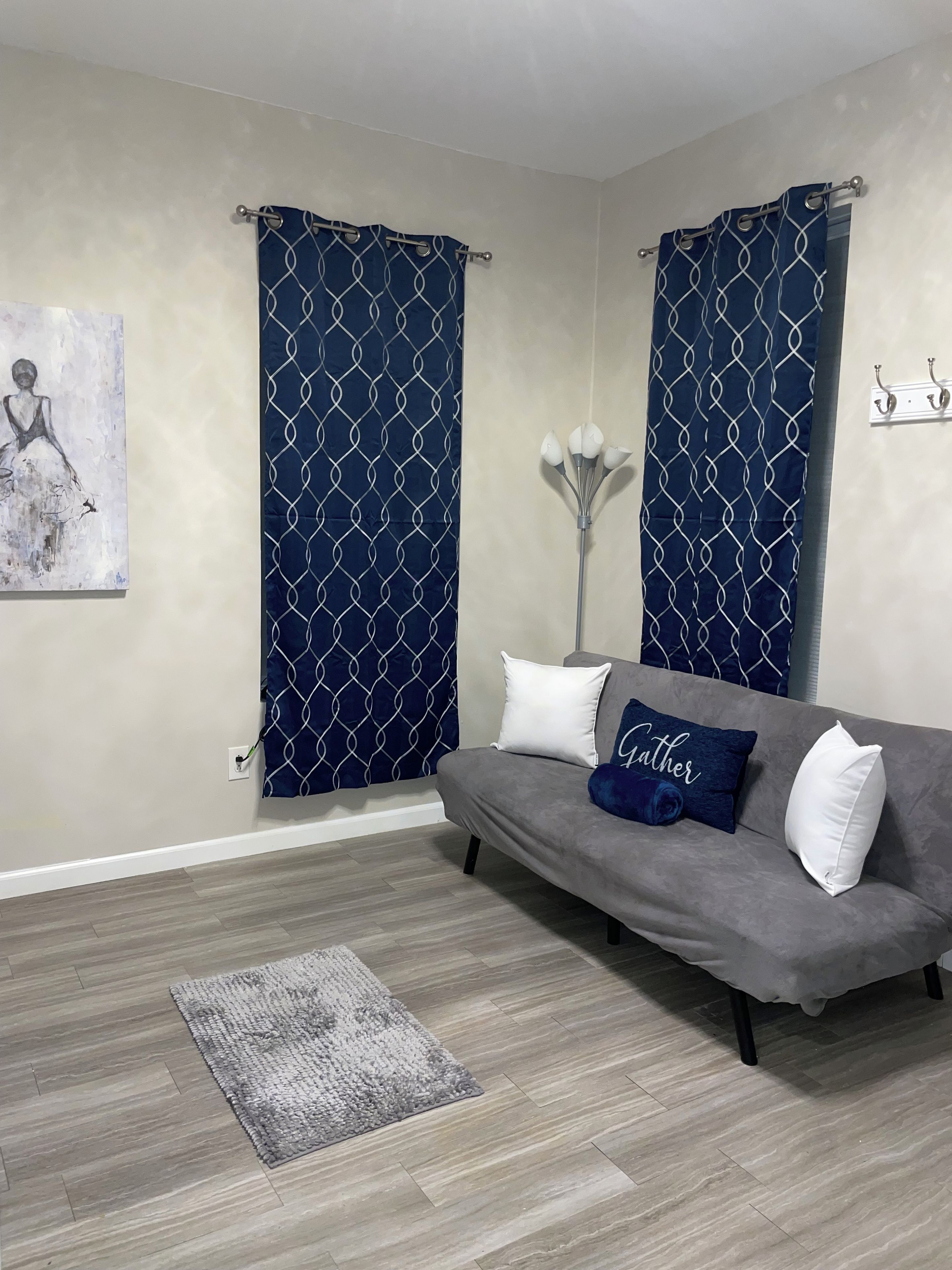 Una sala de estar con un sofá gris, una cortina azul estampada, una alfombra gris y un aplique de pared.