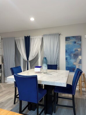 Een eetruimte met een marmeren tafel, blauwe fauteuils en een decoratieve vaas.