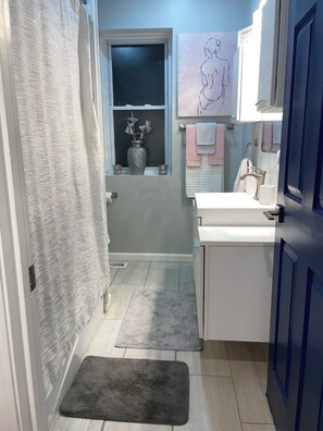 Ein Badezimmer mit Dusche, Waschbecken, Handtuchhalter und einem Fenster mit einer Vase.