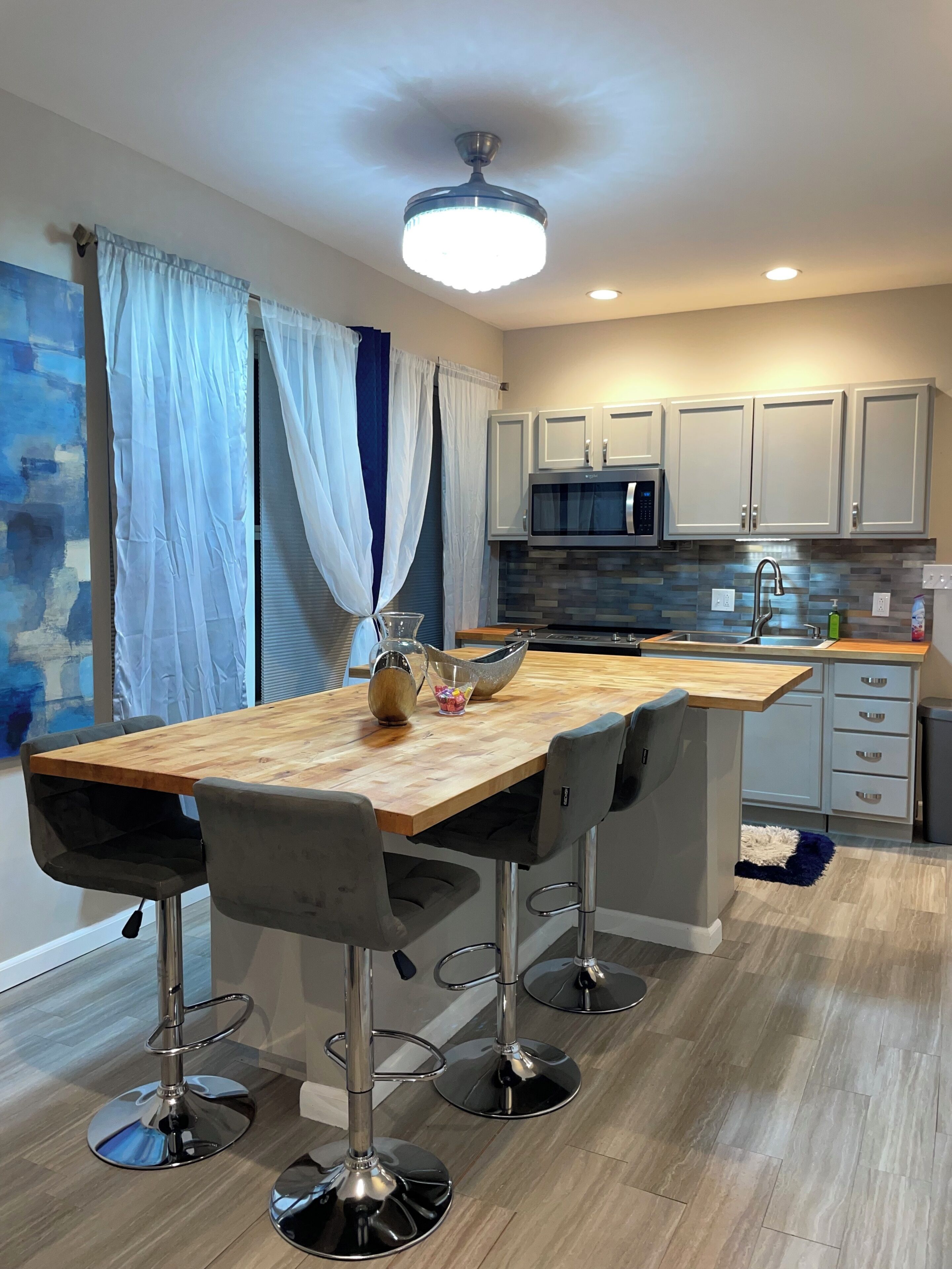 A modern kitchen with a wooden table, bar stools, a microwave, and a sink.