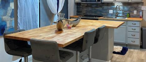 A modern kitchen with a wooden table, bar stools, a microwave, and a sink.