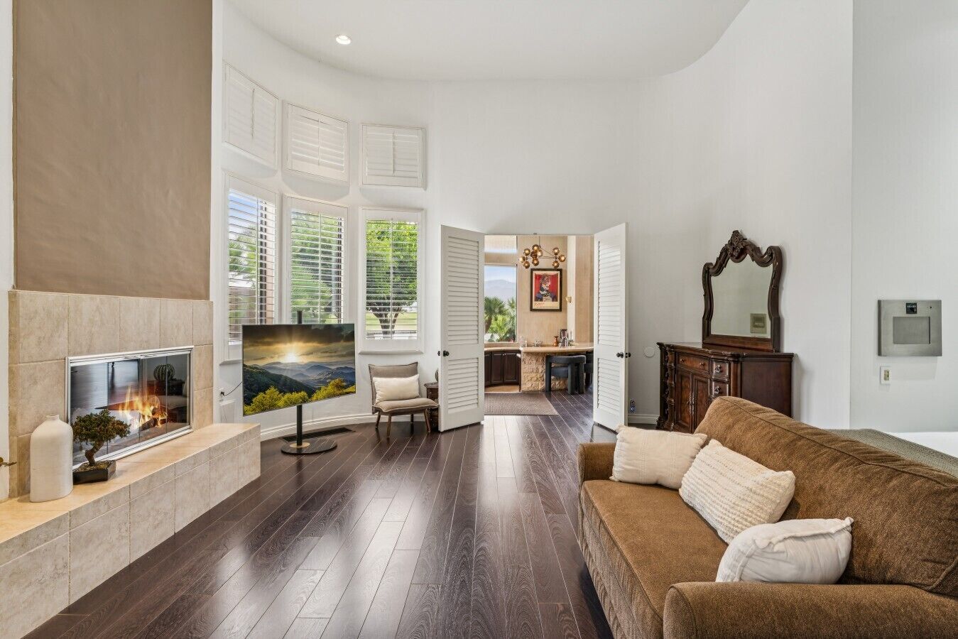 A spacious living room with a fireplace, a flat-screen TV, and a large window overlooking a garden.