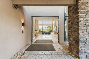 A modern entrance with a stone pathway leading to a glass door, a stone wall on the right, and a view of the interior. - 9th Hole Turn.  On the world famous Stadium Course!  Lake, Golf and MNT Views! (La Quinta)