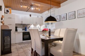 A modern kitchen with white cabinets, a dining table with chairs, and a pendant light. - Holiday Home Godewind with Terrace, Garden, Wi-Fi & Balcony Near Beach in Otterndorf (Otterndorf)