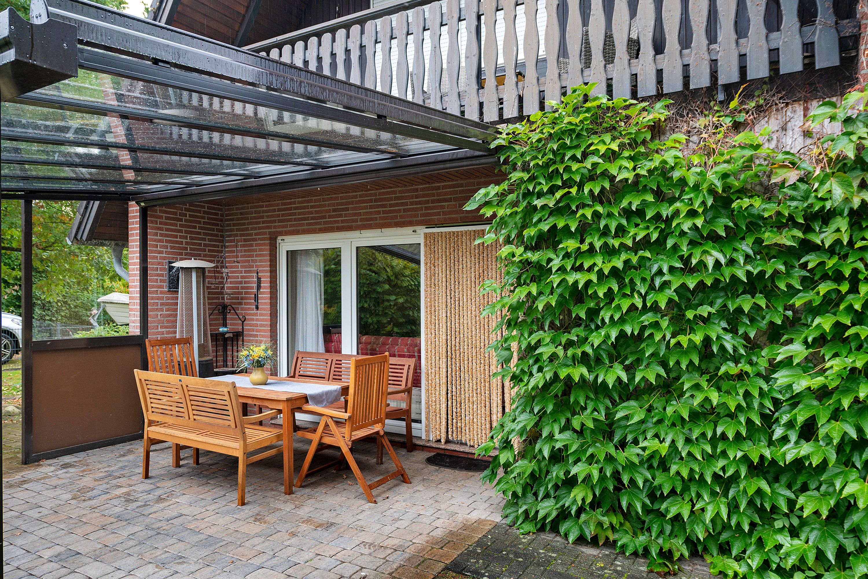 A covered patio with a brick wall, wooden furniture, and a green ivy-covered wall.