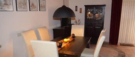 A dining area with a wooden table, white chairs, a black pendant lamp, and a cabinet with glass doors.