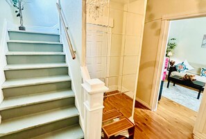 A staircase with white balusters leading to a landing, a chandelier, and a view into a room with a wooden floor and a bed.