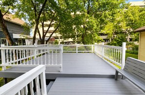 Una terraza de madera con barandillas blancas, rodeada de árboles y edificios.