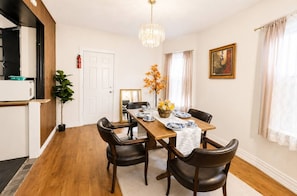 Un comedor con una mesa de madera dispuesta para cuatro personas, rodeada de sillas de cuero oscuro. Un candelabro cuelga del techo y un extintor está montado en la pared.