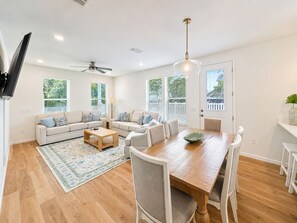 Ein geräumiges Wohnzimmer mit einer Sofagarnitur, einem Esstisch mit Stühlen, einem Holztisch und einem Deckenventilator.