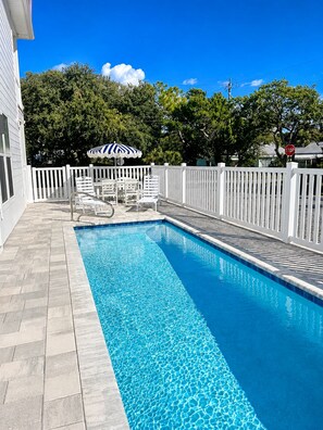 A rectangular swimming pool with a white fence and chairs, surrounded by a white picket fence and trees. - Private Pool + New 4 Bedroom/4.5 Bath Home + Short Walk to the Beach (Panama City Beach)