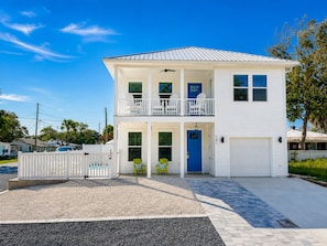 A two-story white house with a blue front door, a balcony on the upper floor, and a garage. - Private Pool + New 4 Bedroom/4.5 Bath Home + Short Walk to the Beach (Panama City Beach)