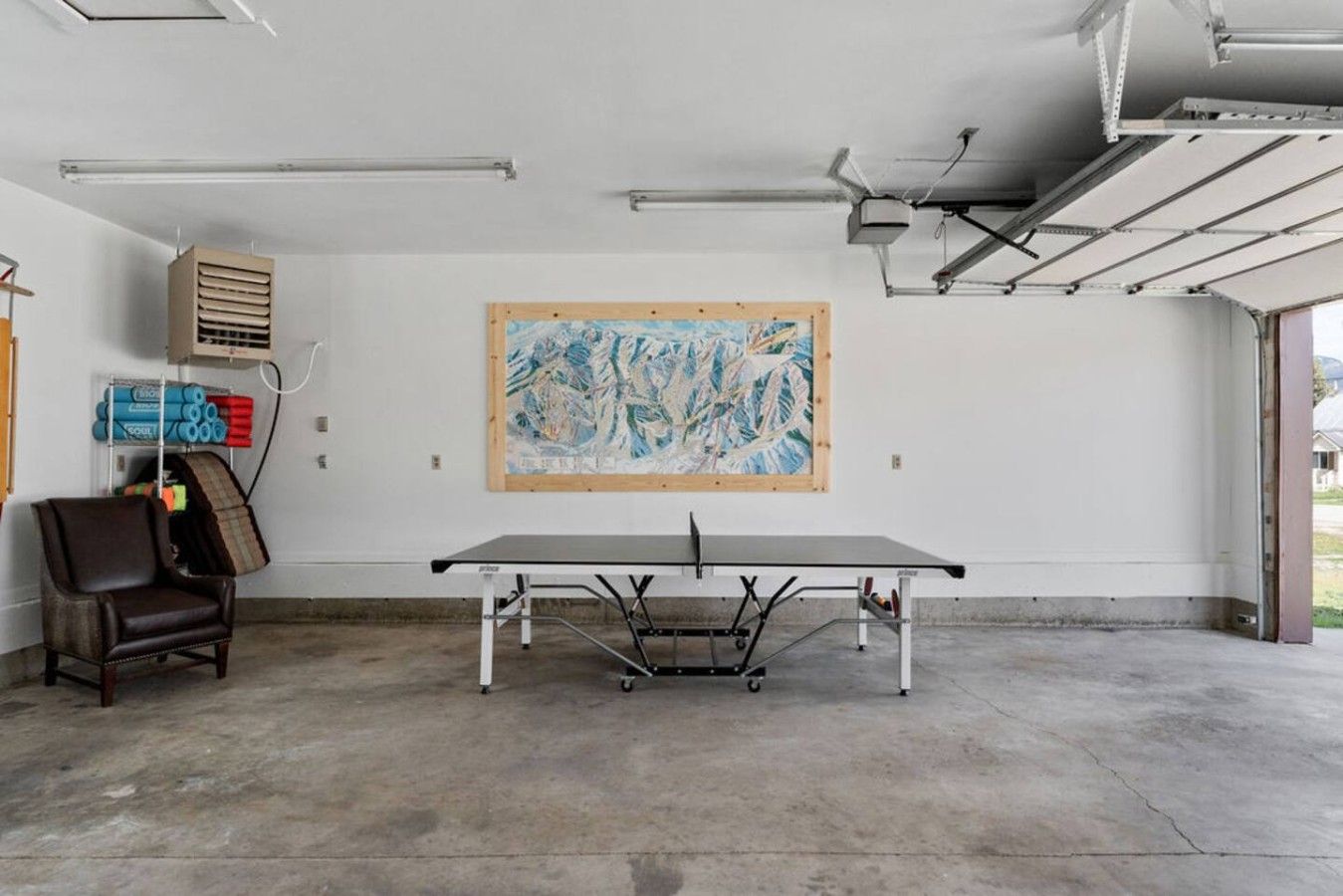 A ping pong table in a room with a large abstract painting on the wall, a chair, and exercise equipment.