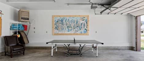Una mesa de ping pong en una habitación con un cuadro abstracto grande en la pared, una silla y equipo de ejercicio.