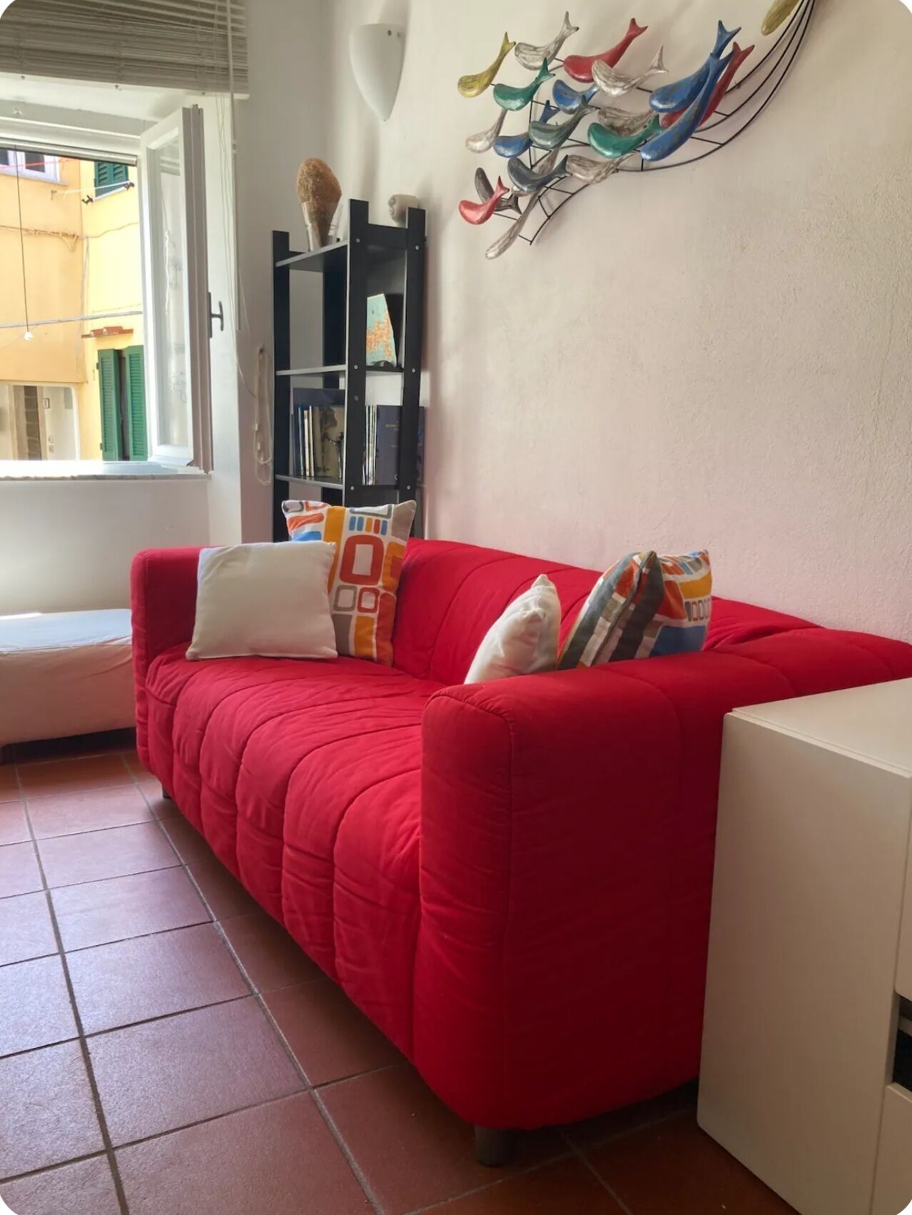A red sofa with a white cushion, a black bookshelf, and a wall-mounted decorative piece.