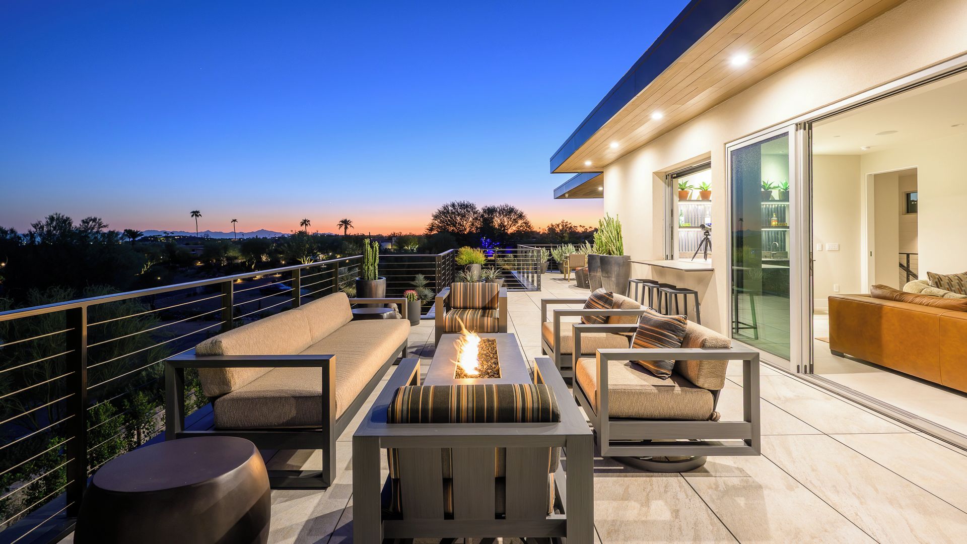 A rooftop terrace with outdoor seating, a fire feature, and a view of the cityscape at dusk.