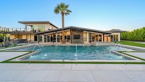 Ein modernes Haus mit Swimmingpool, Gartenmöbeln und einer Palme.