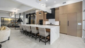 A modern kitchen with a central island, bar stools, pendant lighting, and a dining area with a sofa and chairs. - Luxury 5BR Paradise Valley Estate - Pickleball, Tennis, Basketball Pool, and Spa (Paradise Valley)