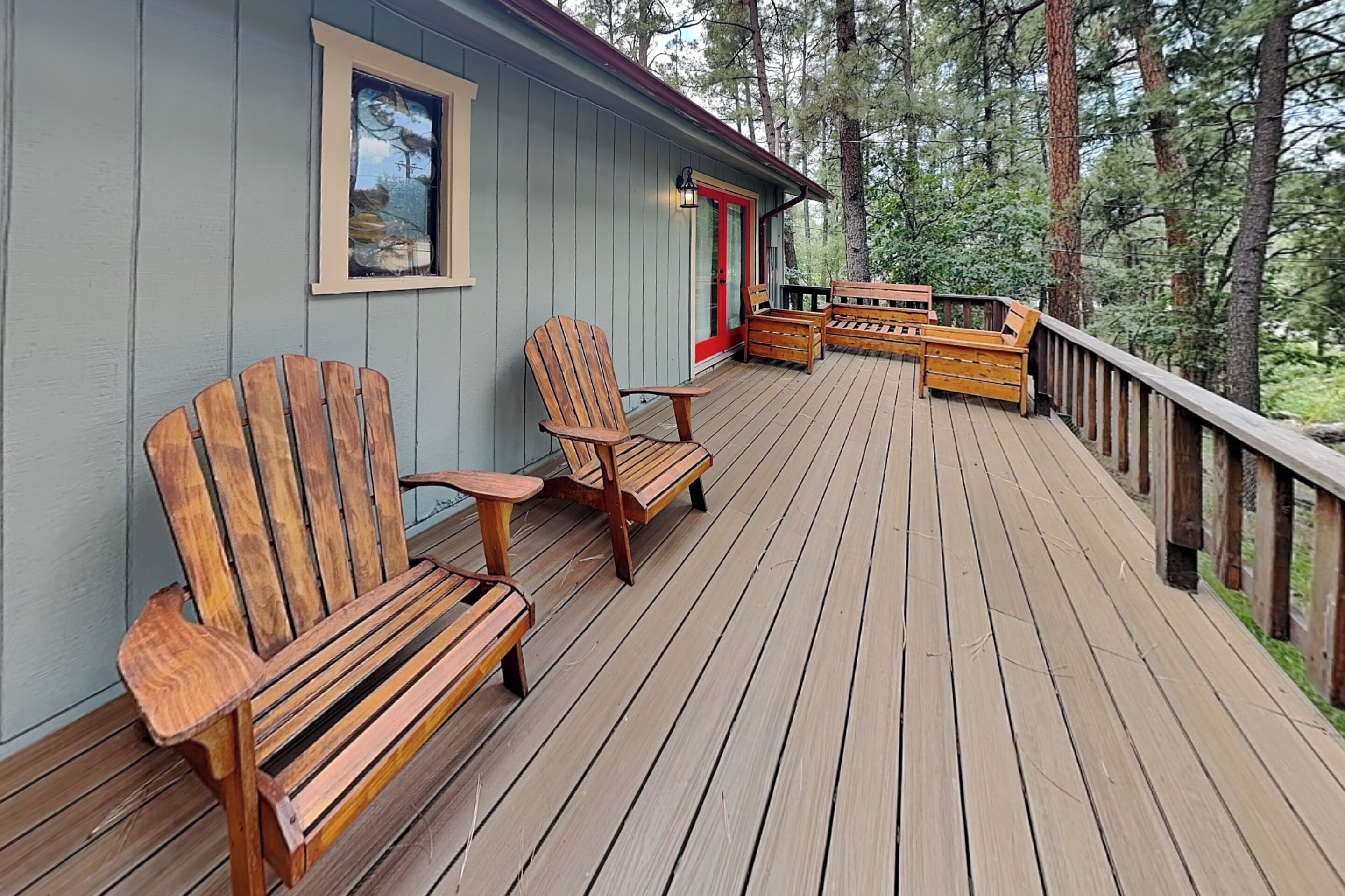 A wooden deck with Adirondack chairs and a bench, surrounded by trees.