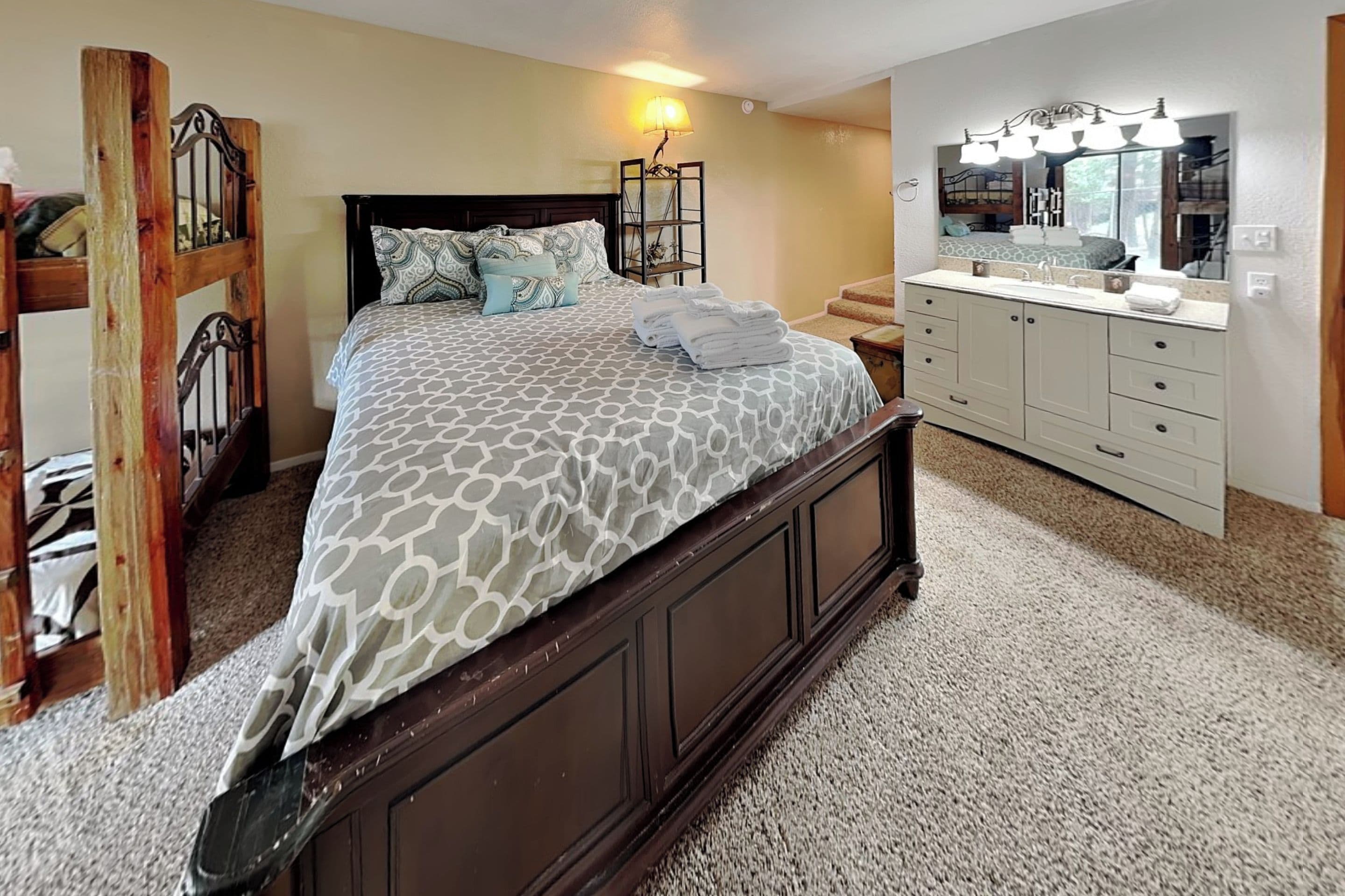 A bedroom with a large bed, a vanity with a mirror, and a staircase leading to an upper level.